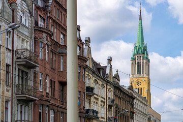 Street view in Łódź featuring historic Art Nouveau tenement houses and the tall spire of the St....