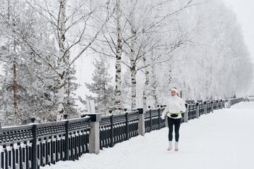 young caucasian woman running in park in winter, white sports jacket, black trousers and small...