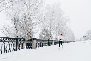 young caucasian woman running in park in winter, white sports jacket, black trousers and small...