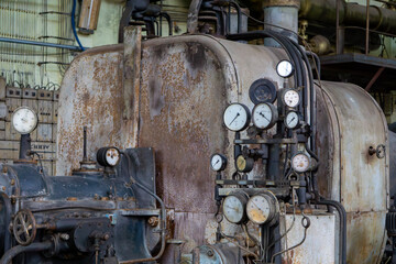Vintage generator in an old power plant, covered in rust and patina, with visible pressure gauges, pipes, and wiring. Industrial interior of a former machine hall with historic technical equipment.