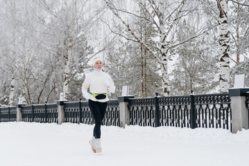 young caucasian woman running in park in winter, white sports jacket, black trousers and small...