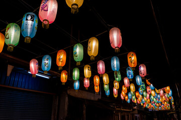 A serene alley illuminated by rows of glowing lanterns suspended above, casting warm light onto the narrow pathway below. The nighttime setting evokes a nostalgic, peaceful mood with traditional cultu