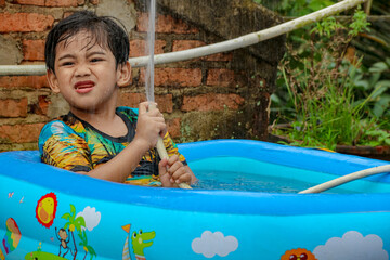 Boy Playing in Kiddie Pool Holding Garden Hose Outdoors