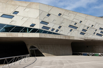 Modern concrete building with geometric asymmetrical windows and futuristic design. Contemporary European architecture, possibly a cultural or exhibition center.