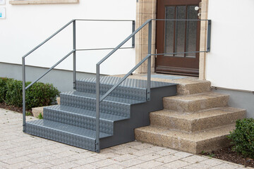 Modern metal stairs with handrails next to old stone steps leading to a building entrance. Concept...