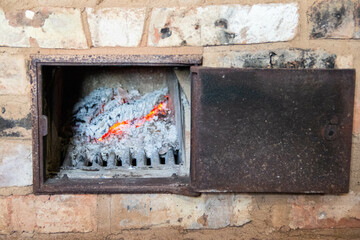 Glowing embers burning in a stove with vivid flames and detailed texture of charred wood and ash. A...