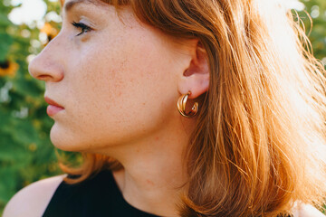 Golden hoop earrings on red-haired woman in sunlight