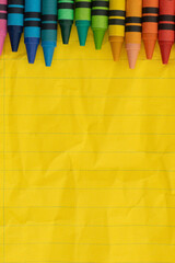 Crayons with yellow ruled loose leaf notebook paper background