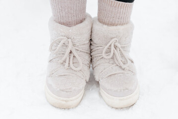 legs in cozy white boots close up, standing on white snow outdoors, trendy fashionable shoes