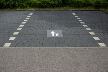 Store parking area with gray paving stones and white markings, including a symbol indicating it is...