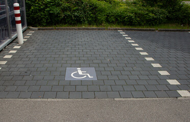 Store parking area with gray paving stones and white markings, including a symbol indicating it is...