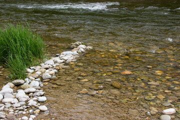 Mountain riverbank in Europe with white stones, rushing clear water, and lush green vegetation along the shores, creating a pristine and vibrant natural landscape.