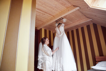 A bride is standing in front of a dress hanging on a rack