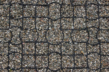 Gravel surface stabilized with a plastic grid, forming a durable, patterned outdoor pavement. Ideal...
