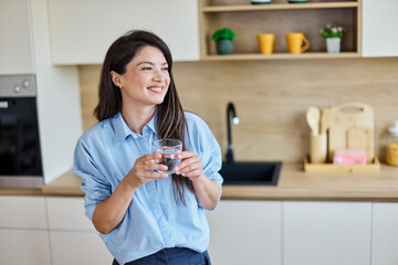 Portrait of a young woman gettyng ready for work drinking a glass of water for hydration standing...