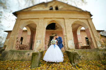 A bride and groom are kissing in front of a building with a large archway
