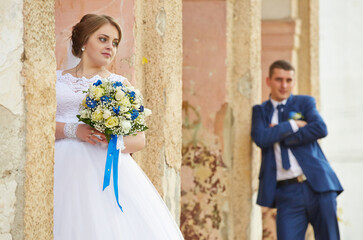 A bride and groom stand in front of a building, with the bride holding a bouquet