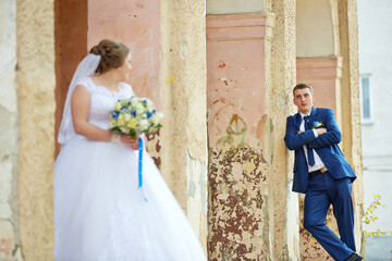 A bride and groom stand in front of a building, with the bride holding a bouquet