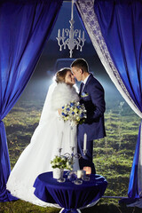 A bride and groom are standing in front of blue curtains