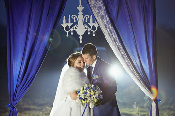 The bride is wearing a white dress and the groom is wearing a blue suit