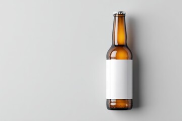 Amber glass beer bottle with blank white label on light grey background; overhead view
