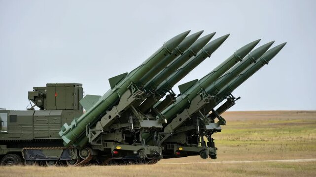 Rows of military missile launchers are positioned on a training ground with a cloudy backdrop. These units are prepared for a drill, highlighting military readiness