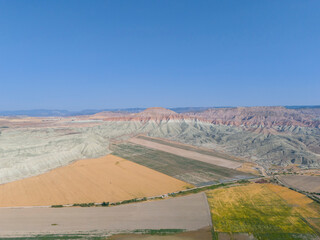 Aerial view of colorful, textured hills and farmland. A high-angle, full shot of a landscape featuring vibrant, multi-hued hills, likely eroded earth formations, contrasting with patches of farmland.