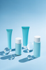 Mockup of blue plastic bottles and tubes with face serum or cream, or toner on blue background with glass balls. The concept of beauty cosmetics, natural products for moisturizing and restoring skin.