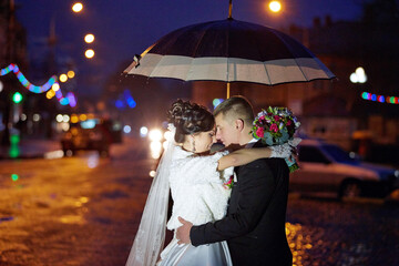 A couple is embracing under an umbrella on a rainy night