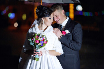 A bride and groom are standing under an umbrella
