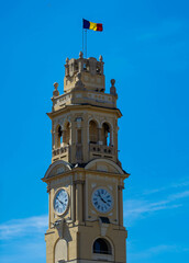 Oradea City Hall Tower in Union Square. Clock tower with the Romanian flag waving in the wind on a blue sky background
