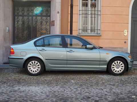 Light green metallic BMW E46 320d sedan with turbodiesel engine, resting on cobblestone street near orange colored historic building facade
