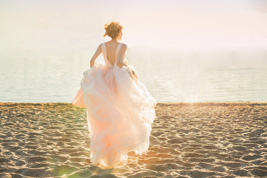 Girl running on the beach in an evening dress. Sunrise by the sea and the bride.