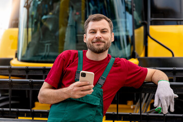 Portrait of farm worker holding smart phone while standing by combine harvester