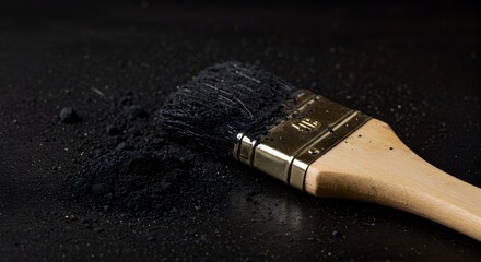 Paintbrush and black charcoal powder scattered on a dark background, symbolizing creativity.