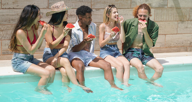 Group of diverse friends enjoying slices of refreshing watermelon while sitting by the pool on a sunny summer day
