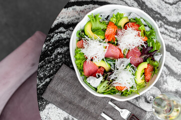 Fresh salad with mixed greens, avocado, grapefruit, tuna, salmon, and daikon in a white bowl,...