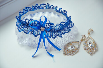 A blue lace train with a white bow is next to a pair of gold earrings