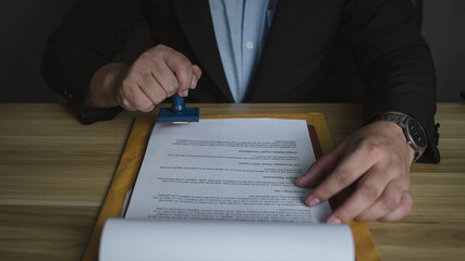 Businessman stamping official document at desk, symbolizing approval, certification, or...