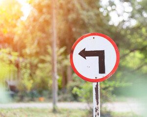 Red and white circular traffic sign with left turn arrow on weathered metal pole against blurred...