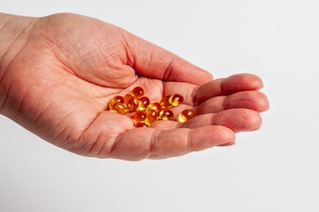 A hand gently holds multiple yellow vitamin d capsules on a white background.