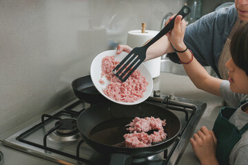 Mother and son cooking ground meat together on stove