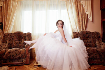 A woman in a white wedding dress is sitting on a couch in a living room