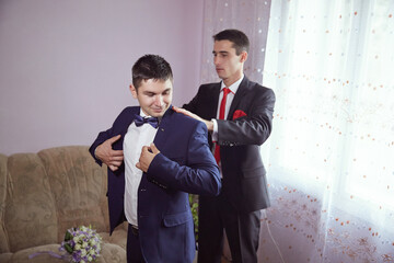 Two men are getting dressed up in a room with a couch in the background