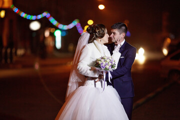 A bride and groom are standing on a street at night