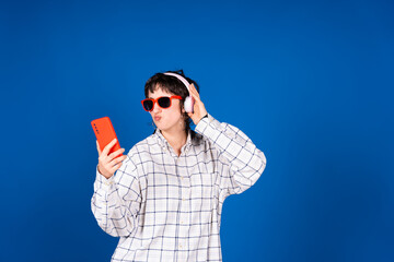 Young stylish woman taking selfie with headphones and smartphone on blue background