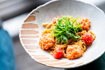 Cooked pasta with tomato sauce, garnished with sesame seeds and herbs, served in a decorative bowl. Appetizing meal presented in vibrant, gourmet style, shot from above.