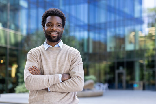 A smiling man stands outside a modern office building, arms crossed.