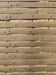 Fragment of ancient wooden door covered with forged uneven metal rusty strips, fixed with forged...