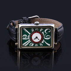 Top view of a rectangular wristwatch with an artistic green dial, expressive typography, and black...